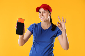 Happy courier with payment terminal showing OK gesture on yellow background