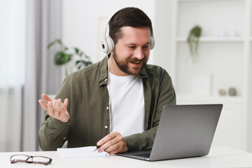Naklejka premium Interpreter in headphones having video chat via laptop at white table indoors