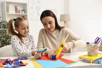 Mother and daughter with hot glue gun and color paper making craft at table indoors