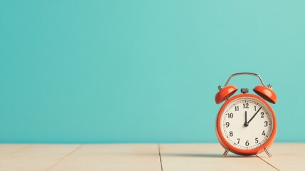 Retro orange alarm clock showing twelve o'clock on light wooden surface against a teal background.