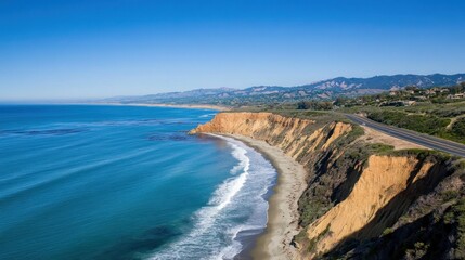 Aerial view of a scenic coastal highway, cliffs, ocean waves, and beach on a sunny day.