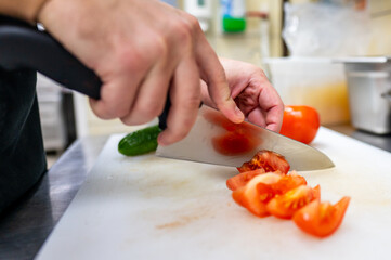 A close-up of hands skillfully slicing a ripe tomato on a white cutting board in a kitchen setting. Fresh vegetables are visible, emphasizing culinary preparation and healthy cooking.