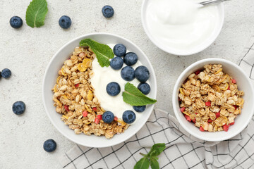 Bowls of tasty granola with yogurt on light grunge background