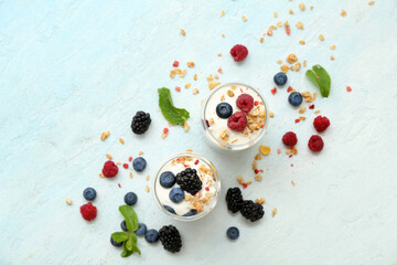 Glasses of tasty granola with yogurt and different berries on pale blue background