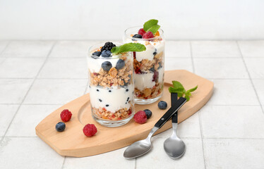 Wooden tray, glasses of tasty granola and yogurt on white tile background