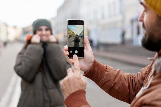 Tourist taking photo of smiling woman with mobile phone in city street