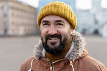 Smiling bearded man wearing yellow beanie and winter jacket in city