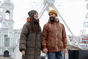 Fototapeta premium Happy couple holding hands and walking near ferris wheel in amusement park