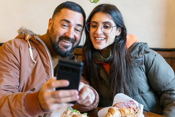 Happy couple enjoying coffee break and browsing smartphone together