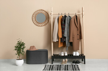 Rack with stylish clothes, pouf and mirror in interior of modern hallway
