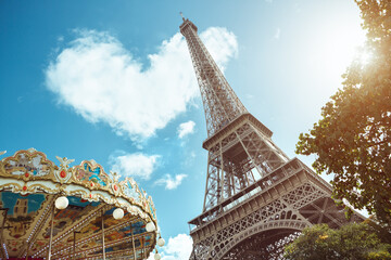 Vivid view of the Eiffel Tower with a charming carousel in the foreground, framed by lush greenery and a bright sunny sky. Perfect for travel, tourism, and cultural projects. © Buyanskyy Production