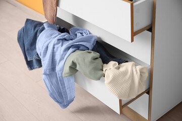 Stylish commode with different scattered clothes, closeup