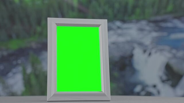 Green screen picture frame standing on surface, blurred waterfall background displaying digital mockup template