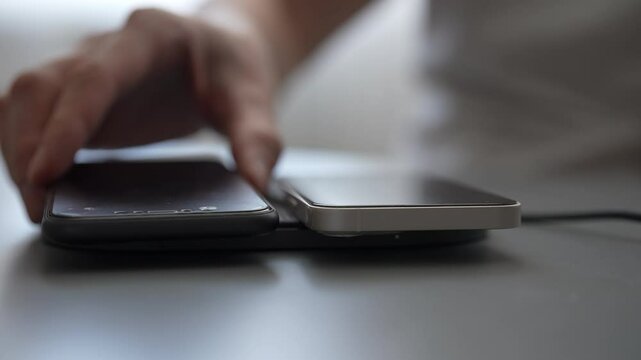 Close-up of male hand positioning smartphone on wireless charging pad, multiple devices charging. Concept of contemporary wireless technology convenience. Shooting in slow motion.