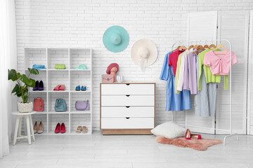 Stylish interior of dressing room with rack, chest of drawers and shelving unit