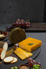 Cheeses in different spices on the table among fruits and greens