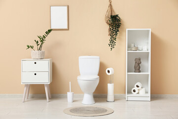 Interior of restroom with toilet bowl, shelving unit and bedside table near beige wall