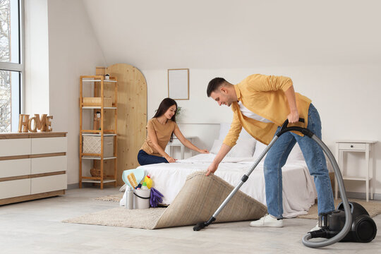 Cute young couple cleaning bedroom together