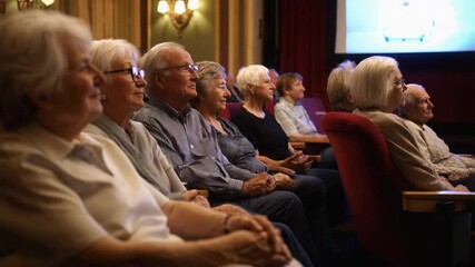 A group of seniors sits attentively in a theater, watching a movie on the big screen. The cozy atmosphere and soft lighting enhance their relaxed expressions