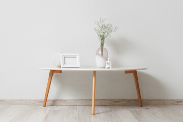 Coffee table with decor and gypsophila flowers in vase near grey wall in room