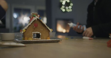 Kids building ginger bread house next to the fireplace. Christmas in family