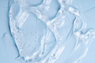 Cosmetic gel or beauty jelly serum texture background. Transparent skin care collagen product backdrop. Antibacterial sanitizer or liquid water moisture toner smudged smear, blue background