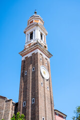 The Campanile dei Santi Apostoli rises 47 meters into the Venetian sky, showcasing its brick façade and prominent clock against a bright blue backdrop in the Cannaregio district.