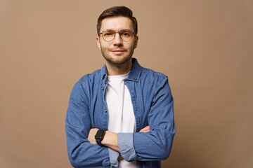 Man in denim shirt poses confidently with arms crossed against a neutral background