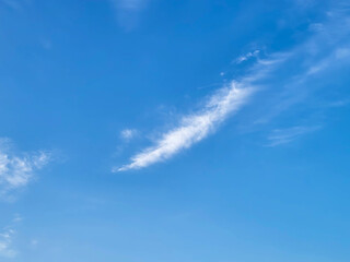 Feathery white fluffy clouds lie against a blue sky background