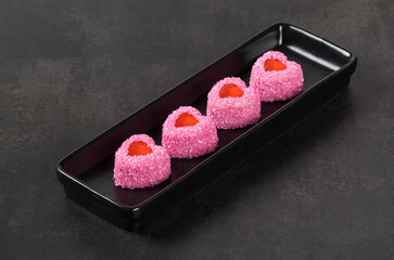 Small Strawberry cream mousse cake with jelly filling, in the shape of a heart, sprinkled with pink coconut chips. On a plate. Dark background. Valentine's day