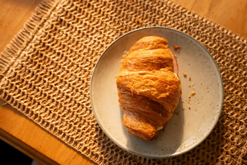 Croissant with ham on woven placemat in sunlight on wooden table