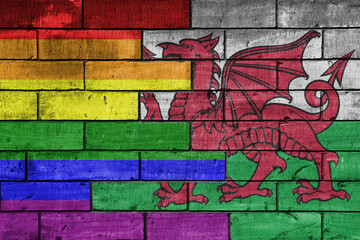colourful painted big flag of wales and rainbow gay pride flag on a massive old brick wall background. concept