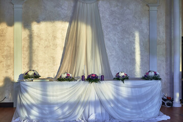 Elegant wedding table with floral arrangements and purple accents, draped white tablecloth,...