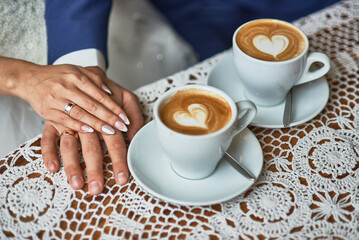 Elegant wedding day image of newlyweds' hands, latte art, crocheted lace tablecloth, romance, two cups, couple's love, heart shape, coffee, unity, special occasion