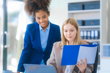 A young African American and Russian woman, both in formal suits, work in a business office. They...