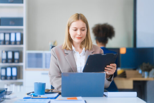 A young Russian woman in formal suit works diligently in business office, analyzing financial charts, using a desktop PC, calculator while contributing to various business strategies and projects.
