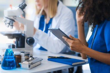 Young African American and Russian woman, both scientists, collaborate to analyze blood samples,...