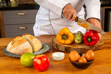 Chef cortando pimentão vermelho em mesa com ingredientes frescos