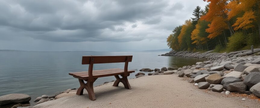 A quiet wooden bench sits atop the rocky shoreline of Pewaukee Lake gazing out onto the serene waters on a cloudy gray day, wisconsin, morning, tranquility