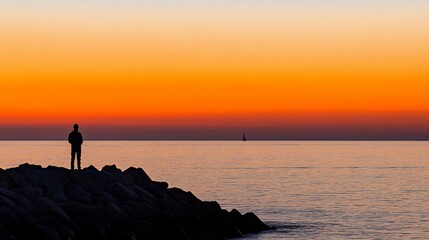 Fototapeta premium Silhouetted man watching sunset over ocean.