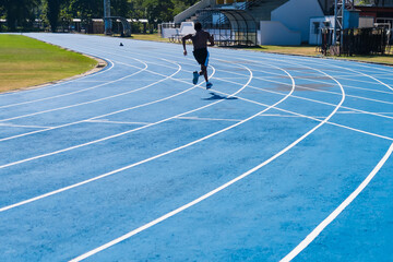 Fototapeta premium Bangkok, Thailand - December, 18, 2024 : Athlete Running on a Blue Synthetic Track in an Outdoor Stadium Under Bright Sunlight for Sports Training at Bangkok, Thailand.