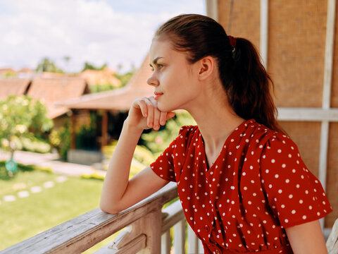 Woman in red polka dot dress gazes wistfully from balcony at scenic view of cityscape