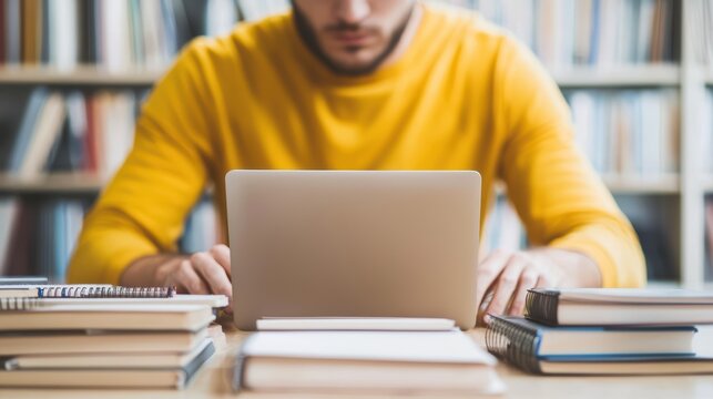A focused individual in a yellow sweater works on a laptop surrounded by books in a cozy library setting and Work from home-remote work.