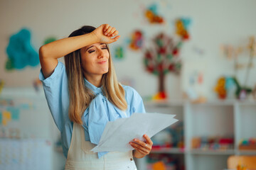 Stressed Kindergarten Teacher Holding Activity Sheets from Students. Overwhelmed educator feeling...