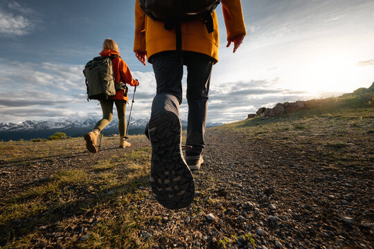 Two young active female hikers tourists girls walks in sunset mountains. Close up photo of woman legs and boots walking in mountains area