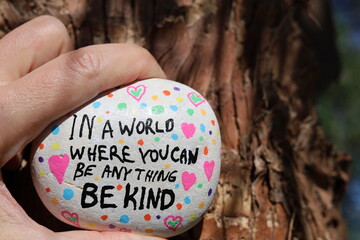 Be kind kindness rock held by tree bark