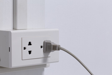 Plug from an electrical appliance. plugged into an electrical outlet on white wall background.