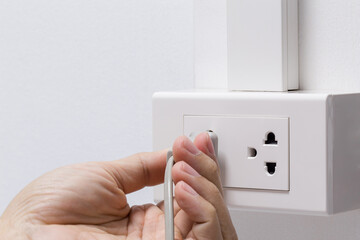 Hand plugging in electric cord into a white socket with white wall. Closeup of a man hand insert electrical plug into wall socket. Keep energy concept.