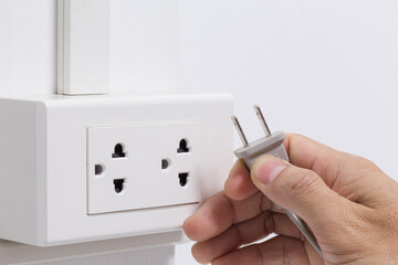 Hand plugging in electric cord into a white socket with white wall. Closeup of a man hand insert electrical plug into wall socket. Keep energy concept.