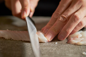 Obraz premium Close-up of hands cutting raw fish with sashimi knife